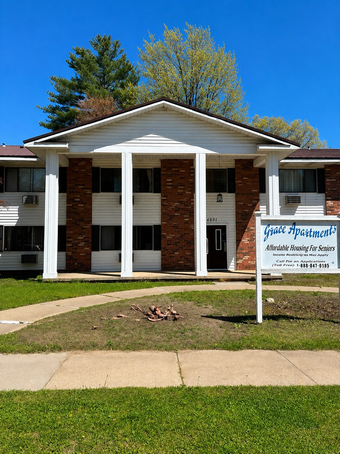 Brick and white apartment building with a sign reading "Spire Apartments" and a large tree nearby, set against a cloudy sky.