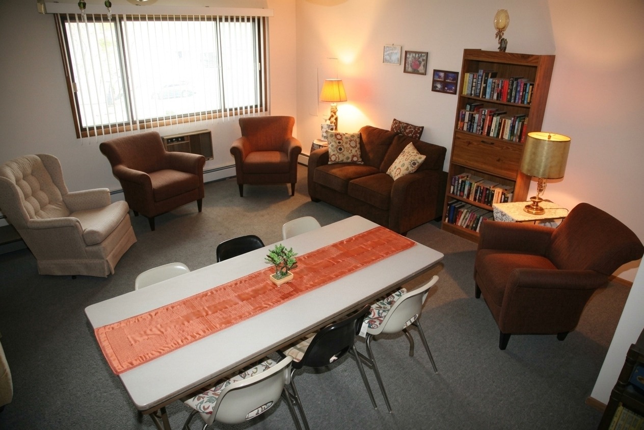 Cozy living room featuring a dining table with eight chairs, a bookshelf filled with books, and comfortable seating arrangements.