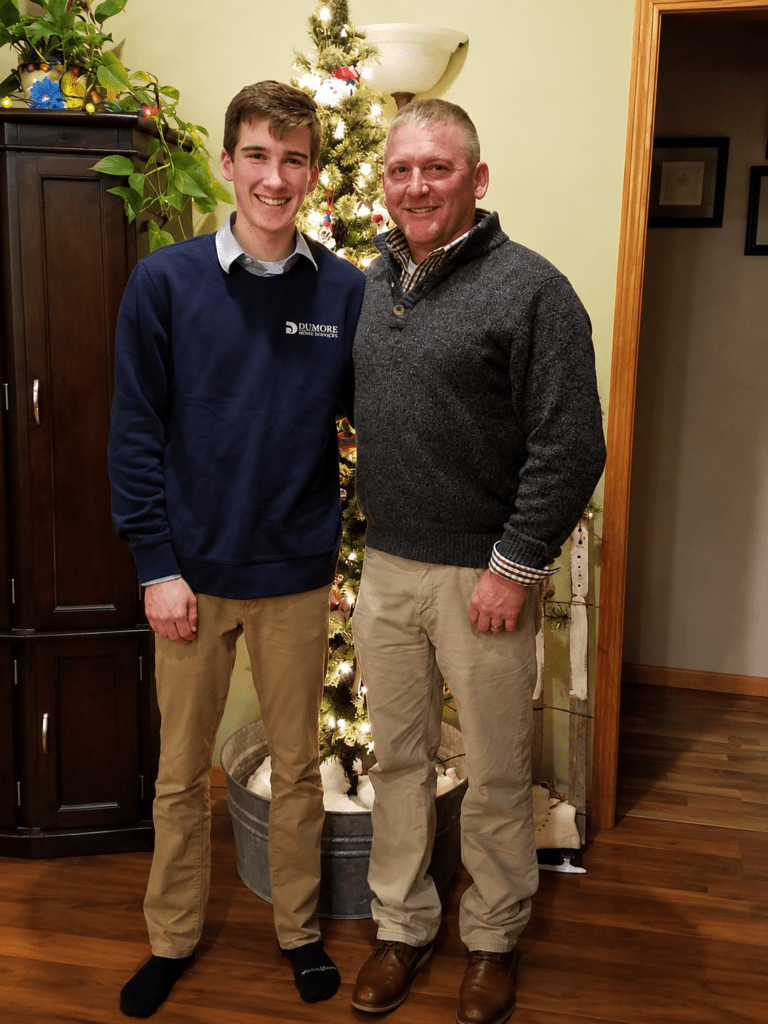 Two men standing together indoors and smiling at the camera